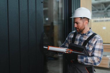 Silikon tabancalı bir işçi modüler bir eve pencere kurduktan sonra boşlukları doldurur.