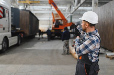 Foreman telsiz kullanarak prefabrik modüler bir evi kamyondan kamyona yüklüyor..