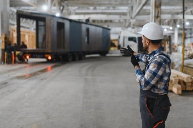 Foreman telsiz kullanarak prefabrik modüler bir evi kamyondan kamyona yüklüyor..
