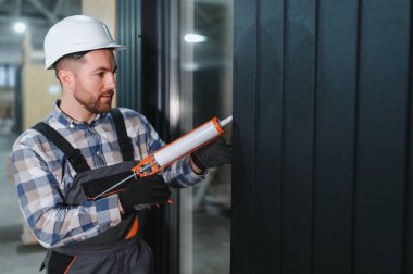 Silikon tabancalı bir işçi modüler bir eve pencere kurduktan sonra boşlukları doldurur.