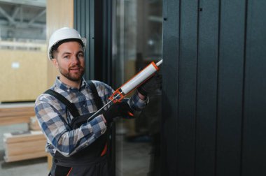 Bir işçi prefabrik modüler evdeki kuşak ve pencere çerçevesi arasındaki boşluğu doldurmak için poliüretan köpük uyguluyor..