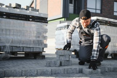 Terasa, yola ya da kaldırıma kaldırım taşları döşeyen inşaat işçisi. Taş kaldırım yapımında taş ve plastik çekiç kullanan bir işçi..