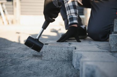 Terasa, yola ya da kaldırıma kaldırım taşları döşeyen inşaat işçilerinin yakın çekimleri. Taş kaldırım yapımında taş ve plastik çekiç kullanan bir işçi..
