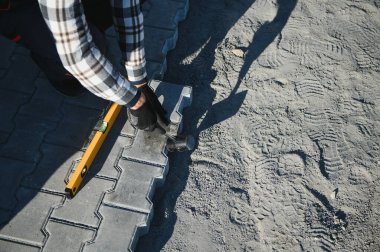 Baharda bahçenin kumlu zeminine kaldırım taşları döşeyen bahçe işçisi. Müteahhit koruyucu bez giyiyor, eldiven takıyor..