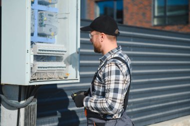 Dış elektrik dağıtım kutusunu tamir eden yetenekli bir inşaat işçisi..
