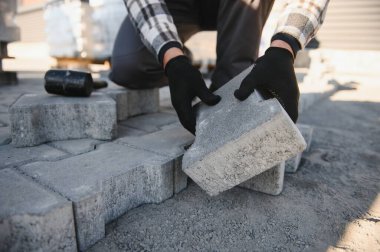 Terasa, yola ya da kaldırıma kaldırım taşları döşeyen inşaat işçilerinin yakın çekimleri. Taş kaldırım yapımında taş ve plastik çekiç kullanan bir işçi..