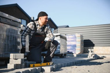 Terasa, yola ya da kaldırıma kaldırım taşları döşeyen inşaat işçisi. Taş kaldırım yapımında taş ve plastik çekiç kullanan bir işçi..