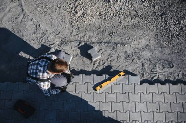 Eldivenlerin ustası katman katman taş döşüyordu. Profesyonel kaldırım işçisi tarafından kaldırım taşı döşenmiş. Kum temeli üzerine ev avlusunda gri beton döşeme döşeme döşeme döşeme.