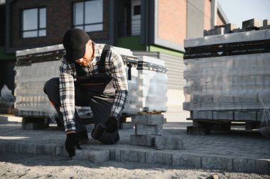 Eldivenlerin ustası katman katman taş döşüyordu. Profesyonel kaldırım işçisi tarafından kaldırım taşı döşenmiş. Kum temeli üzerine ev avlusunda gri beton döşeme döşeme döşeme döşeme.