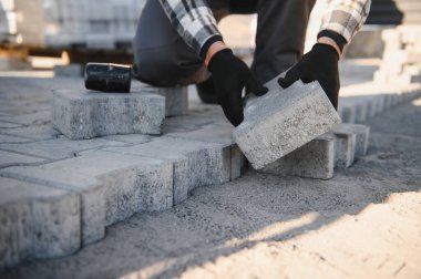 Baharda bahçenin kumlu zeminine kaldırım taşları döşeyen bahçe işçisi. Müteahhit koruyucu bez giyiyor, eldiven takıyor..