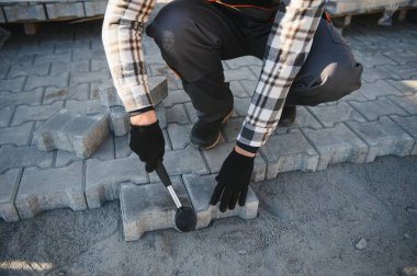 Eldivenlerin ustası katman katman taş döşüyordu. Profesyonel kaldırım işçisi tarafından kaldırım taşı döşenmiş. Kum temeli üzerine ev avlusunda gri beton döşeme döşeme döşeme döşeme.