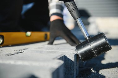 Terasa, yola ya da kaldırıma kaldırım taşları döşeyen inşaat işçilerinin yakın çekimleri. Taş kaldırım yapımında taş ve plastik çekiç kullanan bir işçi..