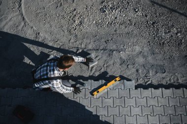Eldivenlerin ustası katman katman taş döşüyordu. Profesyonel kaldırım işçisi tarafından kaldırım taşı döşenmiş. Kum temeli üzerine ev avlusunda gri beton döşeme döşeme döşeme döşeme.