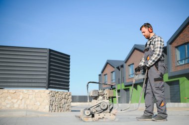 Bahçe düzenleme işçisi, eklemleri doldurmak için Polimerik kum uygulamak için yeni bir veranda kaldırımında titreşimli tamping makinesi plaka sıkıştırıcısı kullanıyor. Ev bahçesi ve peyzaj yenileme projesi geçmişi.
