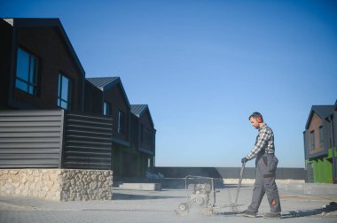 Bahçe düzenleme işçisi, eklemleri doldurmak için Polimerik kum uygulamak için yeni bir veranda kaldırımında titreşimli tamping makinesi plaka sıkıştırıcısı kullanıyor. Ev bahçesi ve peyzaj yenileme projesi geçmişi.