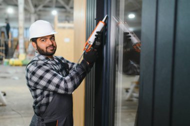 Hintli işçi prefabrik modüler evdeki kuşak ve pencere çerçevesi arasındaki boşluğu doldurmak için poliüretan köpük uyguluyor..