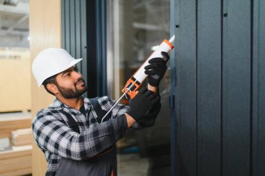 Hintli işçi prefabrik modüler evdeki kuşak ve pencere çerçevesi arasındaki boşluğu doldurmak için poliüretan köpük uyguluyor..