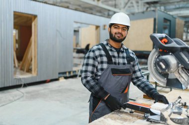 Hintli marangoz, bir modüler yapı fabrikasındaki kereste fabrikasında ahşap bir kereste keserek prefabrik yapı için hassas kesikler sağlıyor.