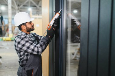 Hintli işçi prefabrik modüler evdeki kuşak ve pencere çerçevesi arasındaki boşluğu doldurmak için poliüretan köpük uyguluyor..