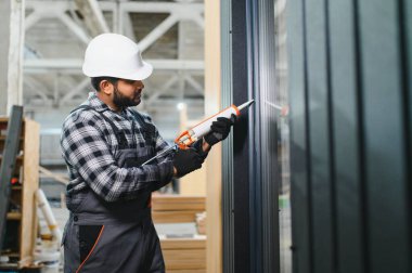 Hintli işçi prefabrik modüler evdeki kuşak ve pencere çerçevesi arasındaki boşluğu doldurmak için poliüretan köpük uyguluyor..