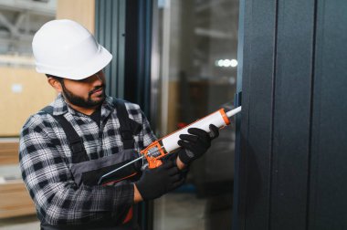 Hintli işçi prefabrik modüler evdeki kuşak ve pencere çerçevesi arasındaki boşluğu doldurmak için poliüretan köpük uyguluyor..