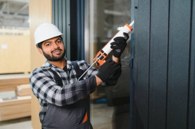 Hintli işçi prefabrik modüler evdeki kuşak ve pencere çerçevesi arasındaki boşluğu doldurmak için poliüretan köpük uyguluyor..