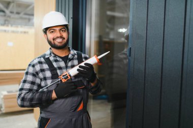 Hintli işçi prefabrik modüler evdeki kuşak ve pencere çerçevesi arasındaki boşluğu doldurmak için poliüretan köpük uyguluyor..