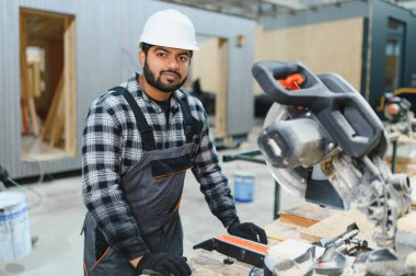 Hintli marangoz, bir modüler yapı fabrikasındaki kereste fabrikasında ahşap bir kereste keserek prefabrik yapı için hassas kesikler sağlıyor.