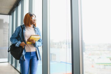 Üniversite koridorunda elinde kitaplarla bekleyen Afrikalı Amerikalı öğrenci..