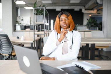 Klinikteki masada dizüstü bilgisayarla çalışan genç Afro-Amerikalı kadın doktor..