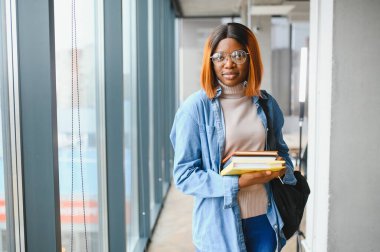 Üniversite koridorunda elinde kitaplarla bekleyen Afrikalı Amerikalı öğrenci..