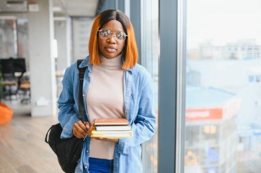 Üniversite koridorunda elinde kitaplarla bekleyen Afrikalı Amerikalı öğrenci..