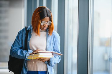 Üniversite koridorunda elinde kitaplarla bekleyen Afrikalı Amerikalı öğrenci..