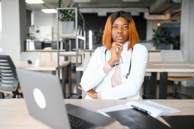 Klinikteki masada dizüstü bilgisayarla çalışan genç Afro-Amerikalı kadın doktor..