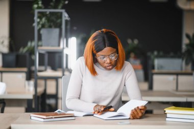 Afrika kökenli Amerikalı kız öğrenci, üniversitenin masasında okuyor. Yüksek öğrenim kavramı.