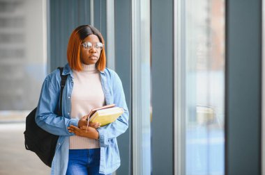 Üniversite koridorunda elinde kitaplarla bekleyen Afrikalı Amerikalı öğrenci..