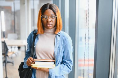 Üniversite koridorunda elinde kitaplarla bekleyen Afrikalı Amerikalı öğrenci..