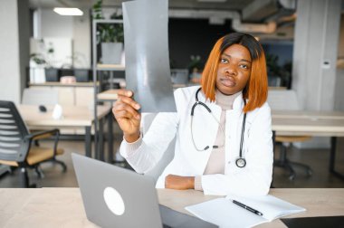 Doktor röntgen çekiyor. Ofisteki genç Afro-Amerikalı doktor röntgene bakıyor..