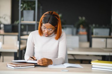 Genç Afrikalı Amerikalı öğrenci üniversitede okuyor, araştırma gazetesinde çalışıyor, açık kitaplarla masada oturuyor..