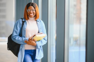 Üniversite koridorunda elinde kitaplarla bekleyen Afrikalı Amerikalı öğrenci..