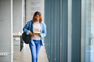 Üniversite koridorunda elinde kitaplarla bekleyen Afrikalı Amerikalı öğrenci..