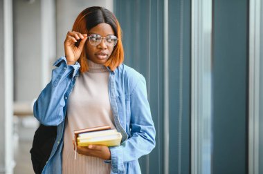 Üniversite koridorunda elinde kitaplarla bekleyen Afrikalı Amerikalı öğrenci..