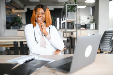 Klinikteki masada dizüstü bilgisayarla çalışan genç Afro-Amerikalı kadın doktor..