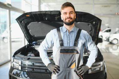 Modern araba tamirhanesinde arabalı dost canlısı bir tamirci. Profesyonel teknisyen araç kontrolü ve bakımını kontrol ediyor. Otomotiv endüstrisi ve müşteri hizmetleri kavramı.