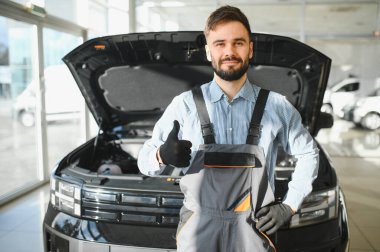 Araba tamircisinin tamirhanesinde tamir edilmiş arabanın yanında baş parmağı görünüyor..