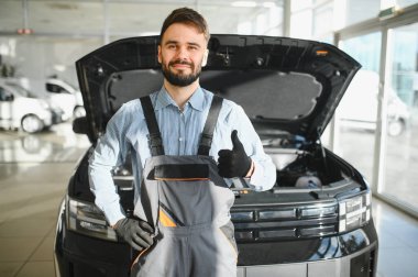 Modern araba tamirhanesinde arabalı dost canlısı bir tamirci. Profesyonel teknisyen araç kontrolü ve bakımını kontrol ediyor. Otomotiv endüstrisi ve müşteri hizmetleri kavramı.