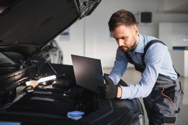 Otomotiv teknisyeni bilgisayarda tanılama yazılımı çalıştırıyor. Tamirci oto servis garajında araç tanılama testi yapıyor..
