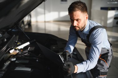 Modern araba tamirhanesinde arabalı dost canlısı bir tamirci. Profesyonel teknisyen araç kontrolü ve bakımını kontrol ediyor. Otomotiv endüstrisi ve müşteri hizmetleri kavramı.