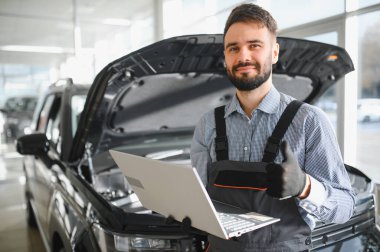 Modern araba tamirhanesinde arabalı dost canlısı bir tamirci. Profesyonel teknisyen araç kontrolü ve bakımını kontrol ediyor. Otomotiv endüstrisi ve müşteri hizmetleri kavramı.