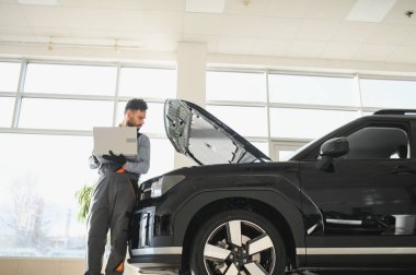 Modern araba tamirhanesinde arabalı dost canlısı bir tamirci. Profesyonel teknisyen araç kontrolü ve bakımını kontrol ediyor. Otomotiv endüstrisi ve müşteri hizmetleri kavramı.